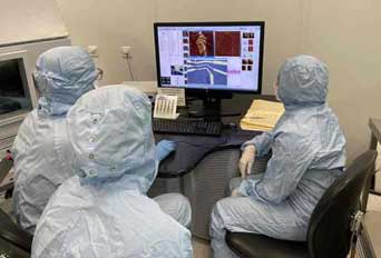 Three researchers wearing lab coats looking at images on a computer monitor