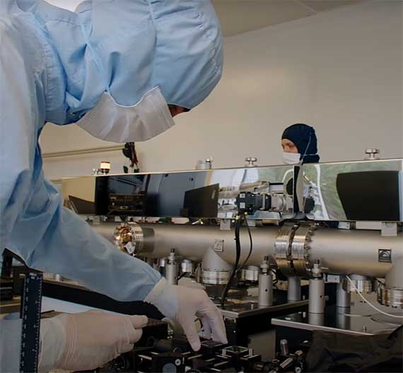 Person operating lab equipment wearing head to toe protective clothing