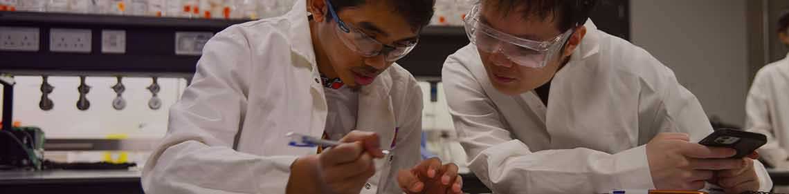 Two people in lab coats at a table working together